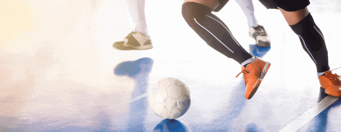 Indoor soccer, football, or futsal player on court, with soccer ball running and kicking with opponent near