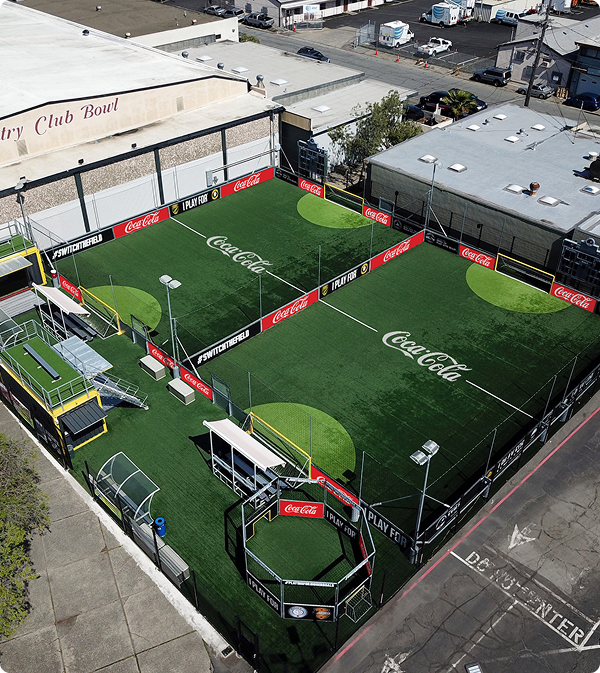 Aerial view of two branded Urban Soccer Park mini-pitches featuring enclosed walls, turf fields, and Coca-Cola sponsor graphics.