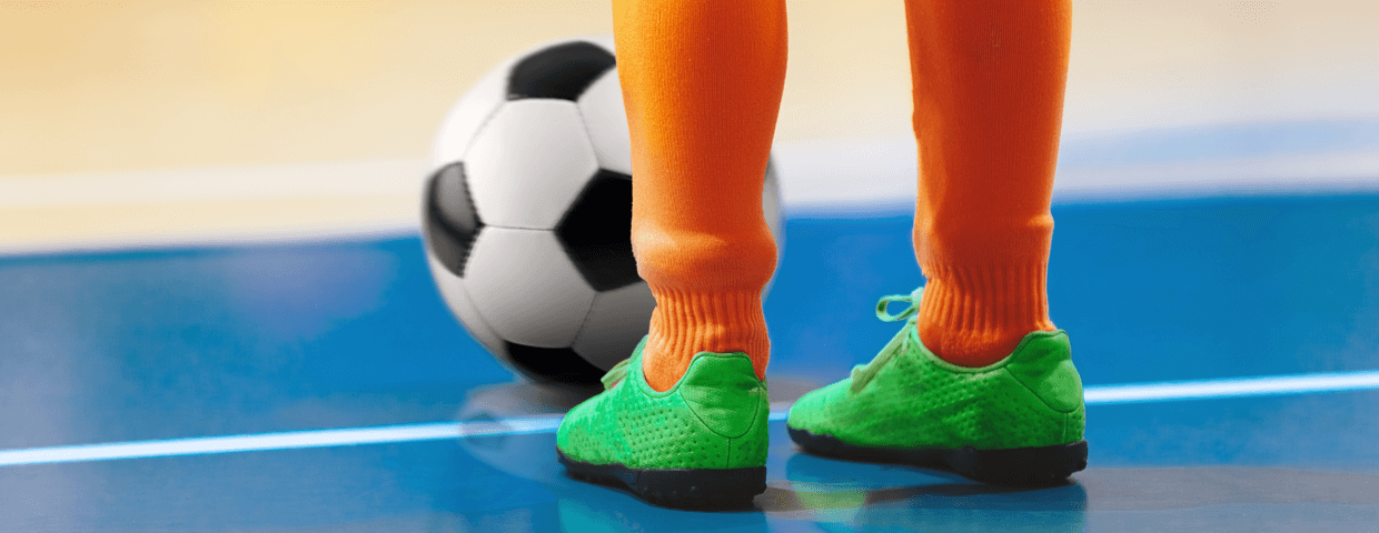 A young kid on a futsal court with his soccer ball. 